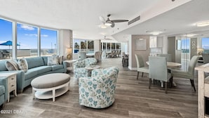 A spacious living area with a large sofa, a round ottoman, and a dining area with chairs and a table.