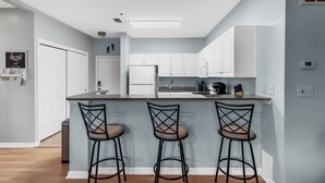 A modern kitchen with white cabinets, a granite countertop, and three bar stools. - North Myrtle Beach Condo (North Myrtle Beach)