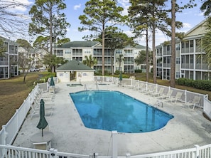 A rectangular swimming pool with a white deck, surrounded by a white fence. There are lounge chairs and umbrellas around the pool.