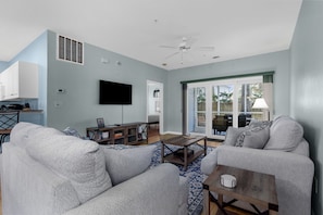 A spacious living room with a gray sofa, a coffee table, and a TV mounted on the wall.