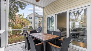A covered patio with a dining table and chairs, a sofa, and a glass door leading to an indoor living area. - North Myrtle Beach Condo (North Myrtle Beach)