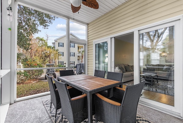 A covered patio with a dining table and chairs, a sofa, and a glass door leading to an indoor living area.