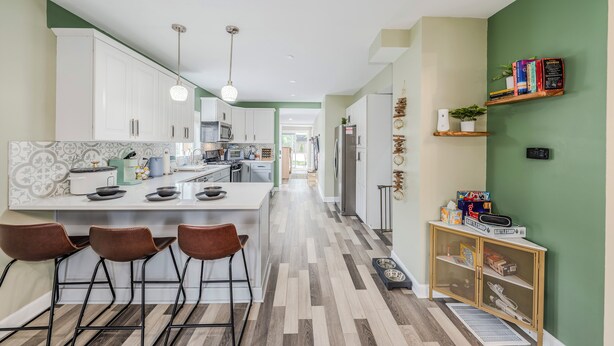 Una cucina moderna con mobili bianchi, un'isola centrale con sgabelli e una parete verde a contrasto.