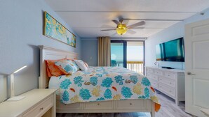 A bedroom with a bed, a ceiling fan, a TV, and a view of the ocean.