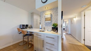 A modern kitchen with a stone backsplash, a coffee maker, a toaster, and a bar stool. - Ocean View, Shared Pool/Hot Tub, Boardwalk to Beach (Port Aransas)