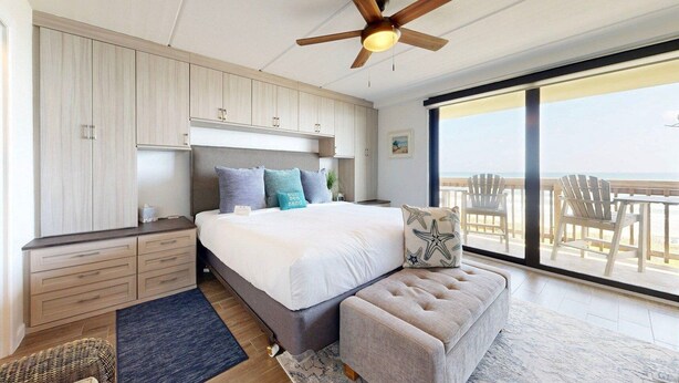 A bedroom with a large bed, a ceiling fan, a view of the beach, and a balcony with chairs. - Ocean View, Shared Pool/Hot Tub, Boardwalk to Beach (Port Aransas)