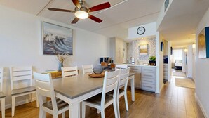 A modern kitchen with white cabinetry, a dining area with a wooden table and white chairs, and a ceiling fan with red blades. - Ocean View, Shared Pool/Hot Tub, Boardwalk to Beach (Port Aransas)