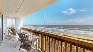 Ein Balkon mit Holzgeländern und Adirondack-Stühlen mit Blick auf einen Strand und Wellen.