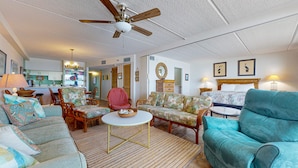 Ein geräumiges Wohnzimmer mit Deckenventilator, Essbereich mit Stühlen, einer Couch und einem Bett mit Kopfteil.