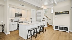 Una cocina moderna con armarios blancos, un refrigerador de acero inoxidable y una isla central con taburetes de bar.