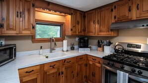 A kitchen with wooden cabinets, a stainless steel stove, a microwave, and a window providing natural light. - Modern Chalet w/ Serene Views and Jacuzzi Hot Tub- 15 Minutes to Okemo Mountain (Chester)