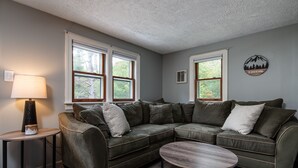 A modern living room with a sectional sofa, a round coffee table, and a lamp on a side table. - Modern Chalet w/ Serene Views and Jacuzzi Hot Tub- 15 Minutes to Okemo Mountain (Chester)
