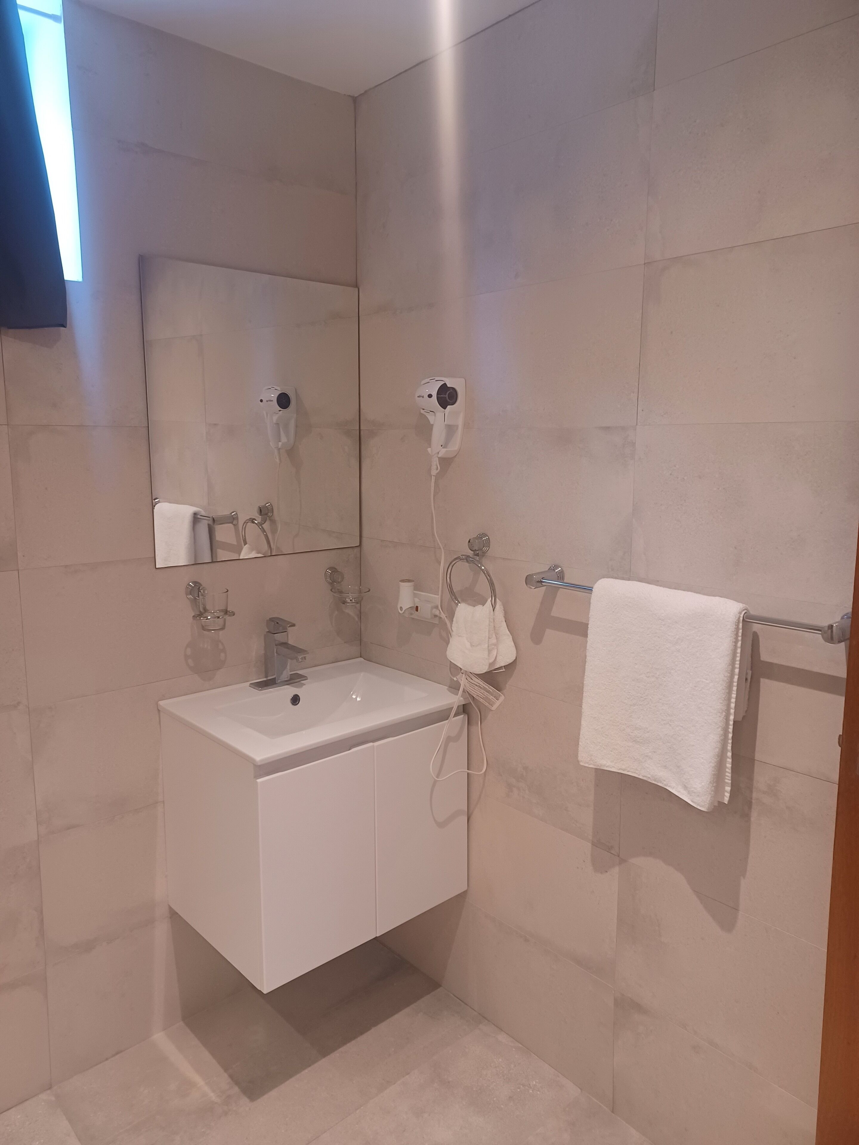 A bathroom with a white sink, a mirror, a towel rack, and a hairdryer mounted on the wall.