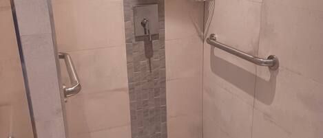 A walk-in shower with a glass door, a handrail, and a tiled floor.