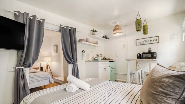 A hotel room with a bed, a desk, a kitchenette, and a TV. - 4 Beach Flats Sleeps 18 2Blks from Beach,Boardwalk,Sand,Surf (San Diego)