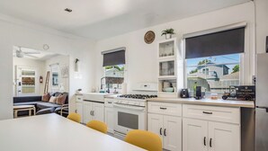 A modern kitchen with white cabinets, a gas stove, and a dining area with a table and chairs. - 4 Beach Flats Sleeps 18 2Blks from Beach,Boardwalk,Sand,Surf (San Diego)