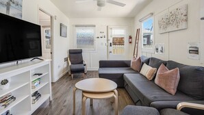 A modern living room with a flat-screen TV, a grey sofa with cushions, a wooden coffee table, and a ceiling fan. - 4 Beach Flats Sleeps 18 2Blks from Beach,Boardwalk,Sand,Surf (San Diego)