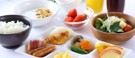 A breakfast table with various food items including rice, eggs, sausages, and fruits.