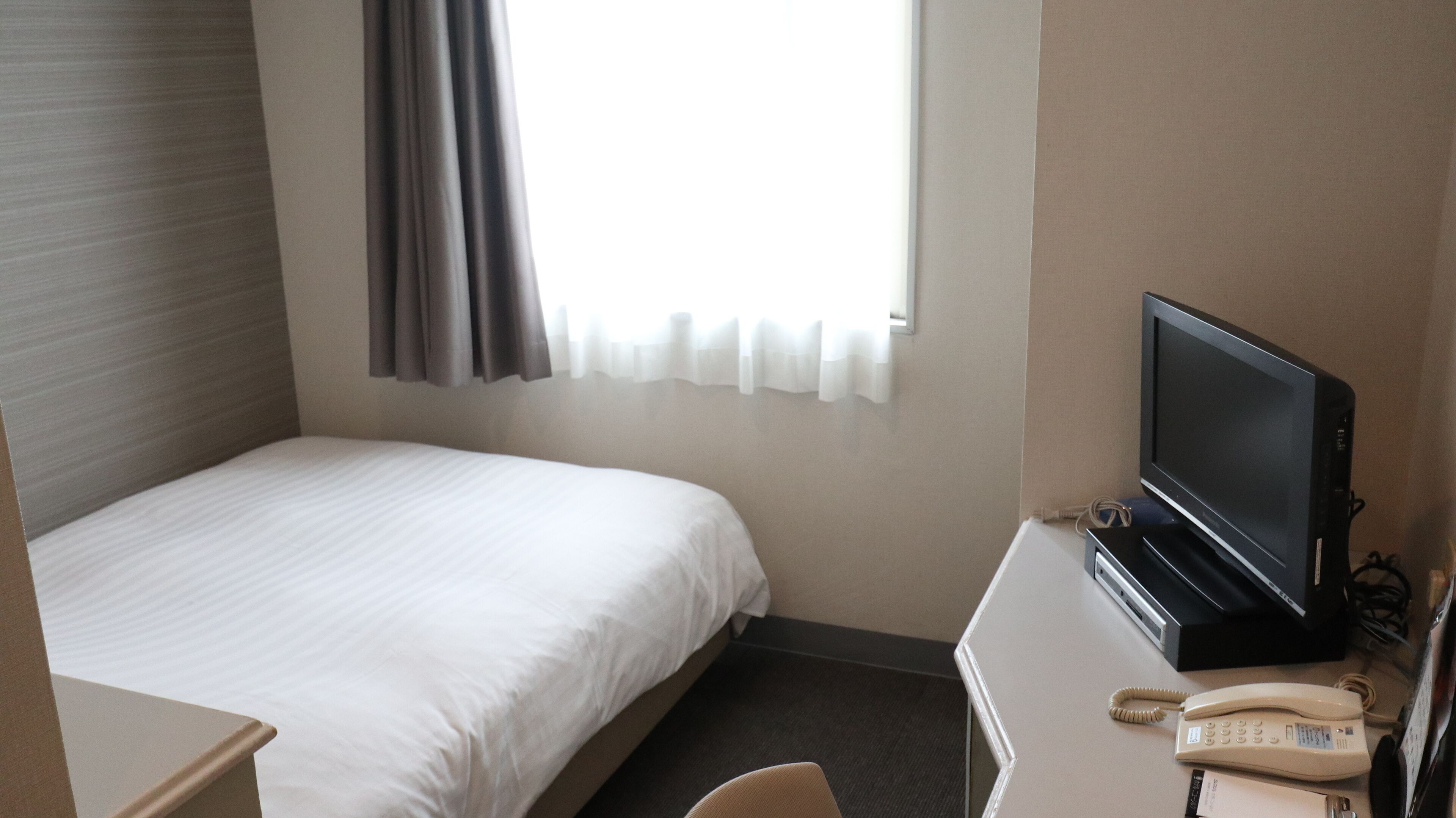 A hotel room with a bed, a desk with a television, a telephone, and a window with curtains.