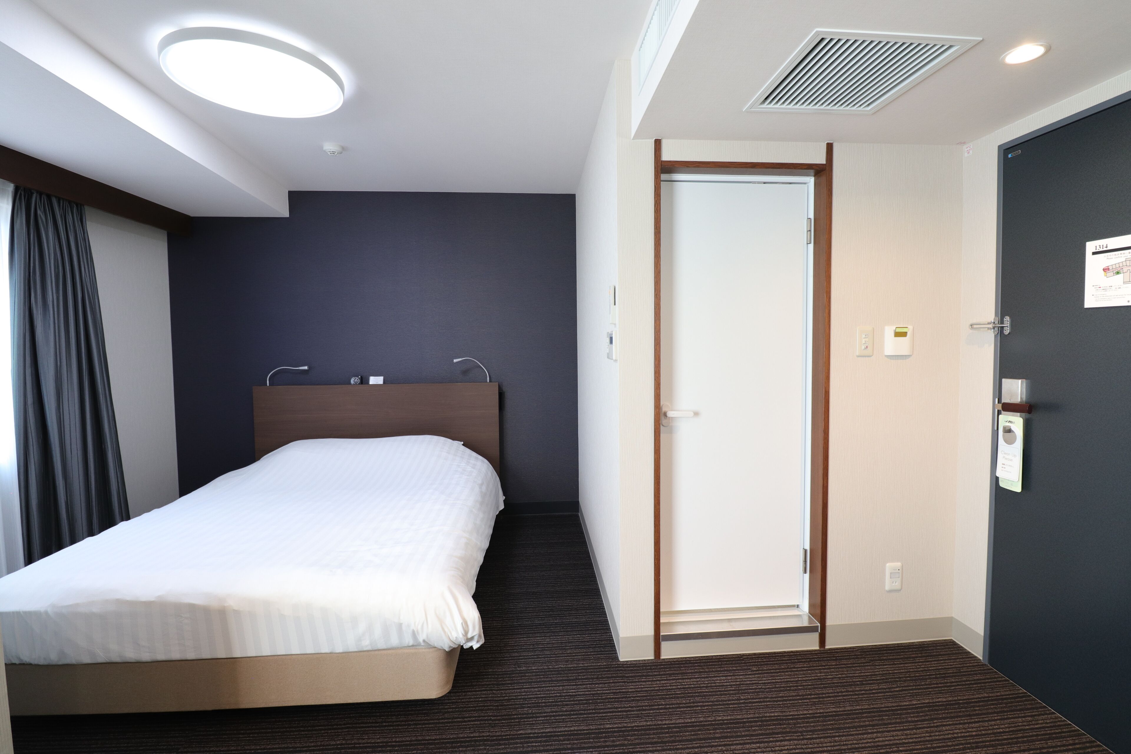 Et hotelværelse med en seng, en dør og en loftslampe.