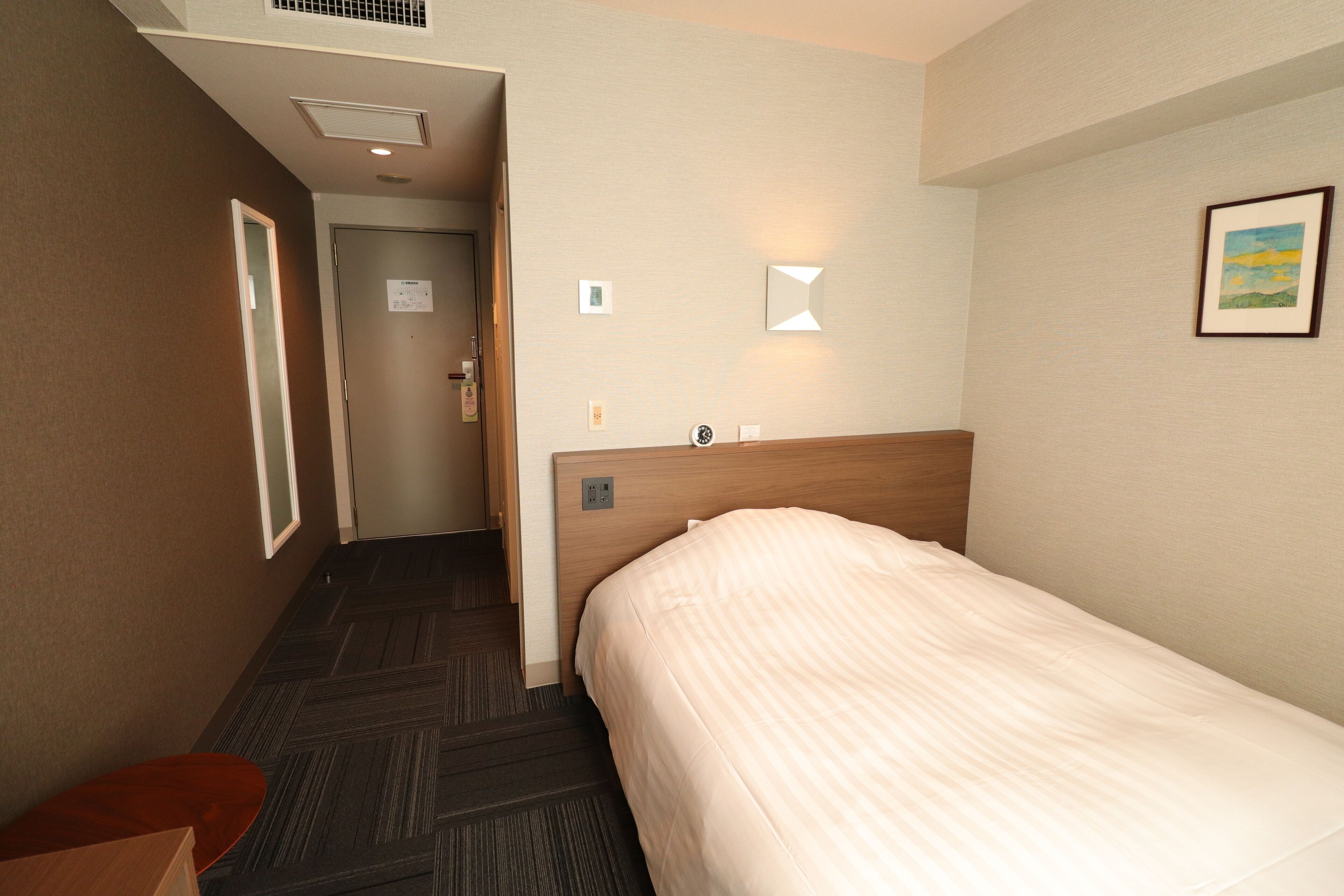 A hotel room with a bed, a small table, a mirror, and a picture on the wall.