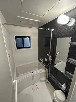 Een moderne badkamer met een badkuip, douche, toilet en een raam.