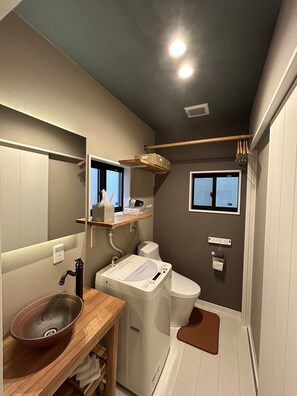 Een compacte badkamer met een houten wastafelmeubel, een inbouw wastafel, toilet en een klein raam.