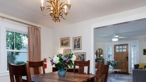 A dining room with a wooden table, chairs, a chandelier, and a patterned rug.