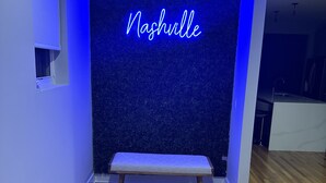 Una habitación con un banco, una pared con la palabra “Nashville” iluminada y piso de madera.