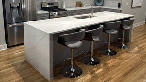 Una cocina moderna con una isla central, electrodomésticos de acero inoxidable y taburetes de bar.