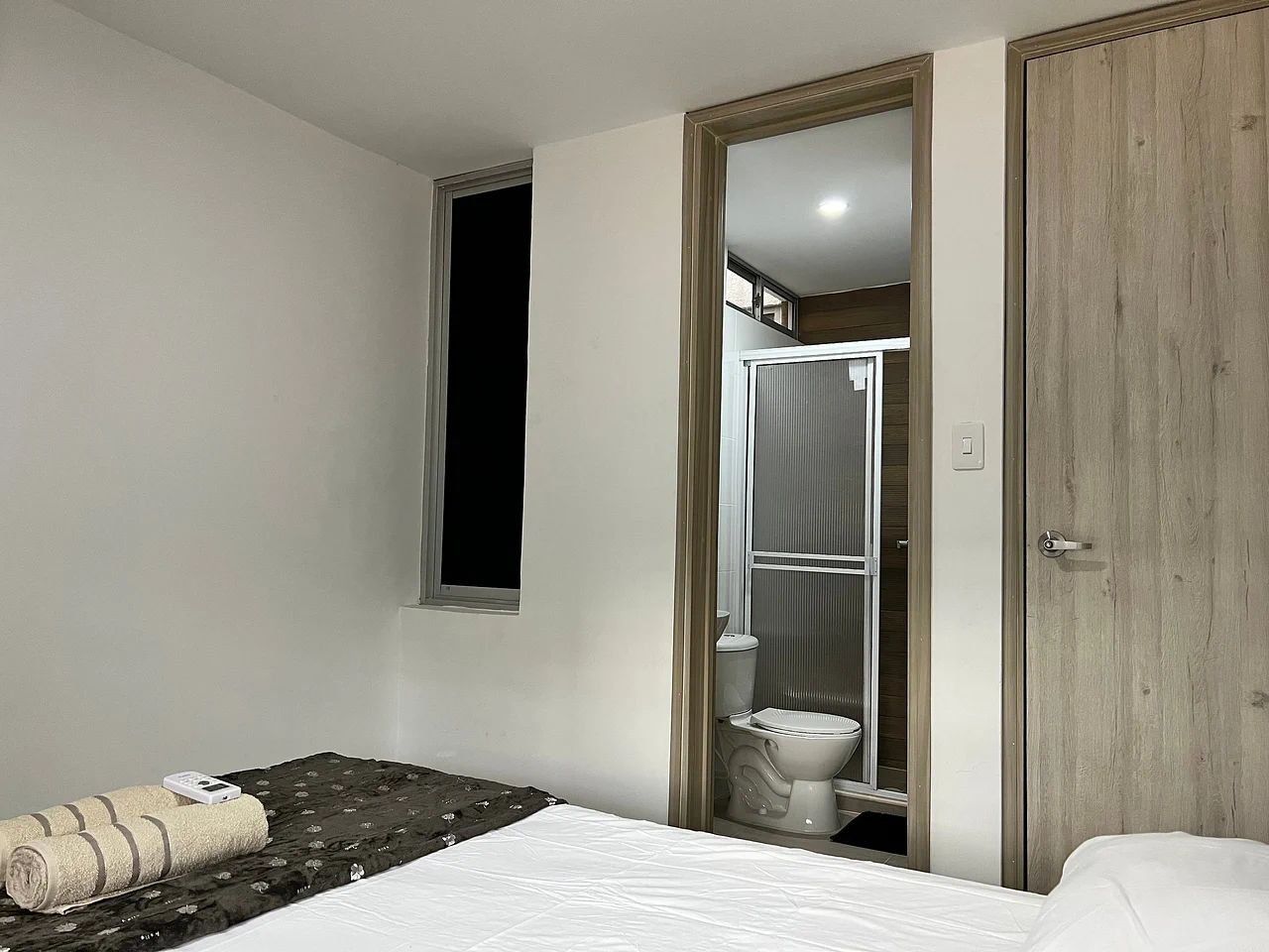 Un dormitorio con cama, ventana, puerta y vistas al baño.