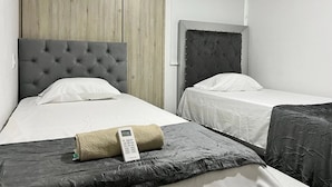 A hotel room with two beds, a wooden wardrobe, and a bedside table with a remote control.
