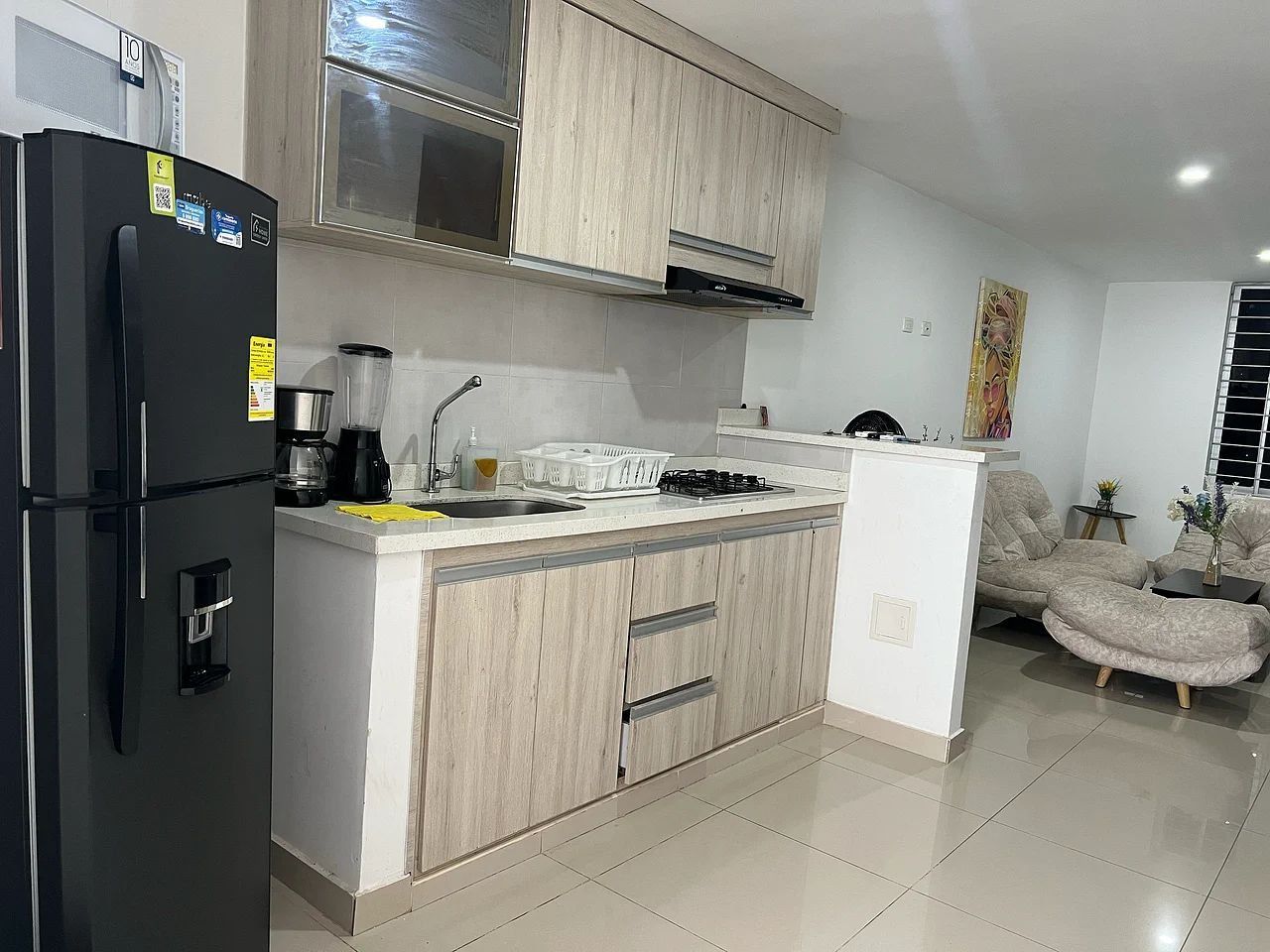A modern kitchen with a refrigerator, stove, and sink. There is a small island with a sink and a chair.