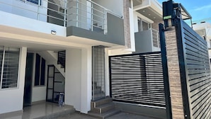 A modern two-story house with a balcony, a gated entrance, and a staircase leading to the upper floor.