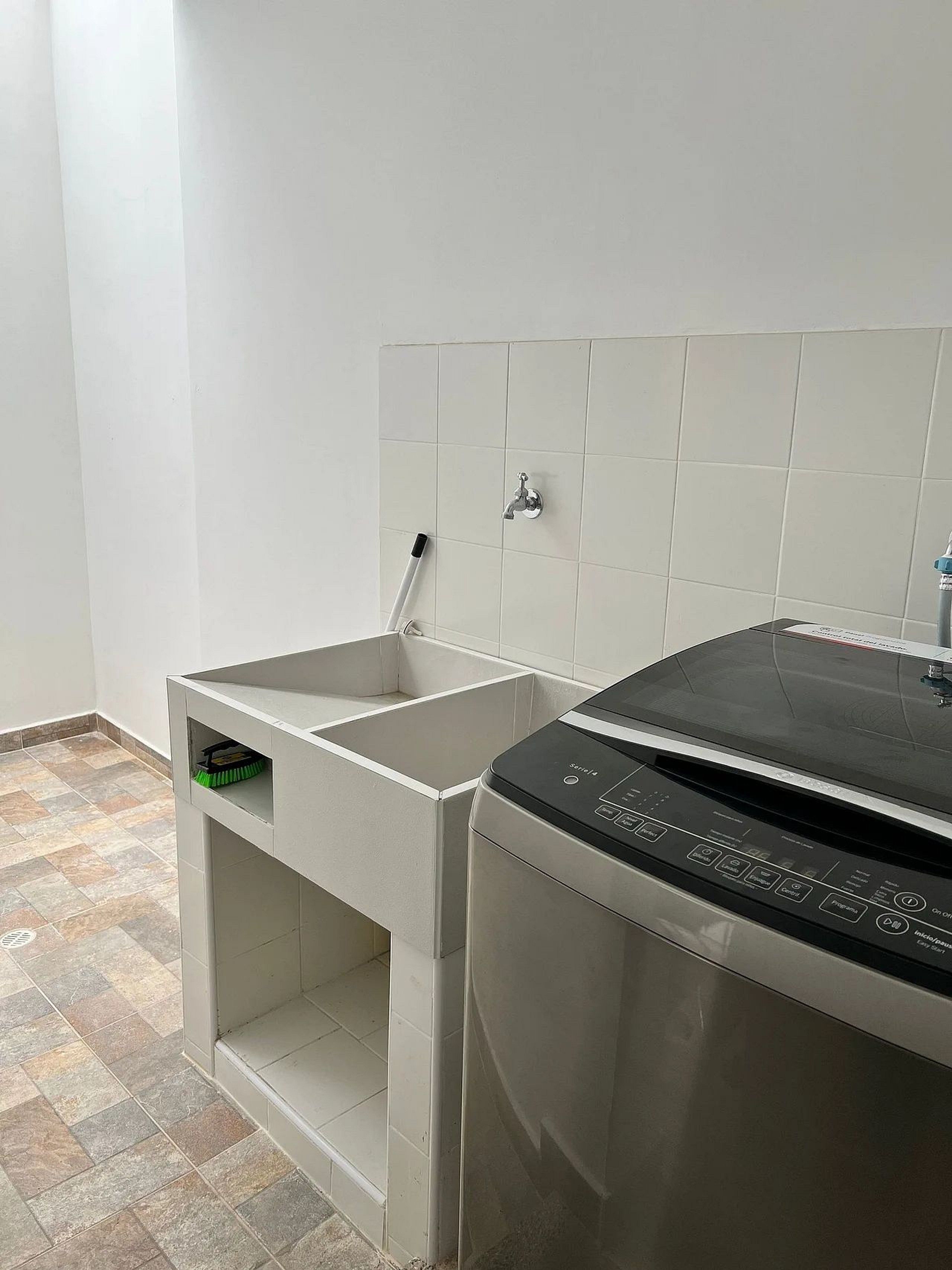 A compact kitchen with a dishwasher, a broom, and a tiled backsplash.