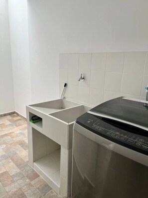Cocina compacta con lavavajillas, escoba y salpicadero de azulejos.