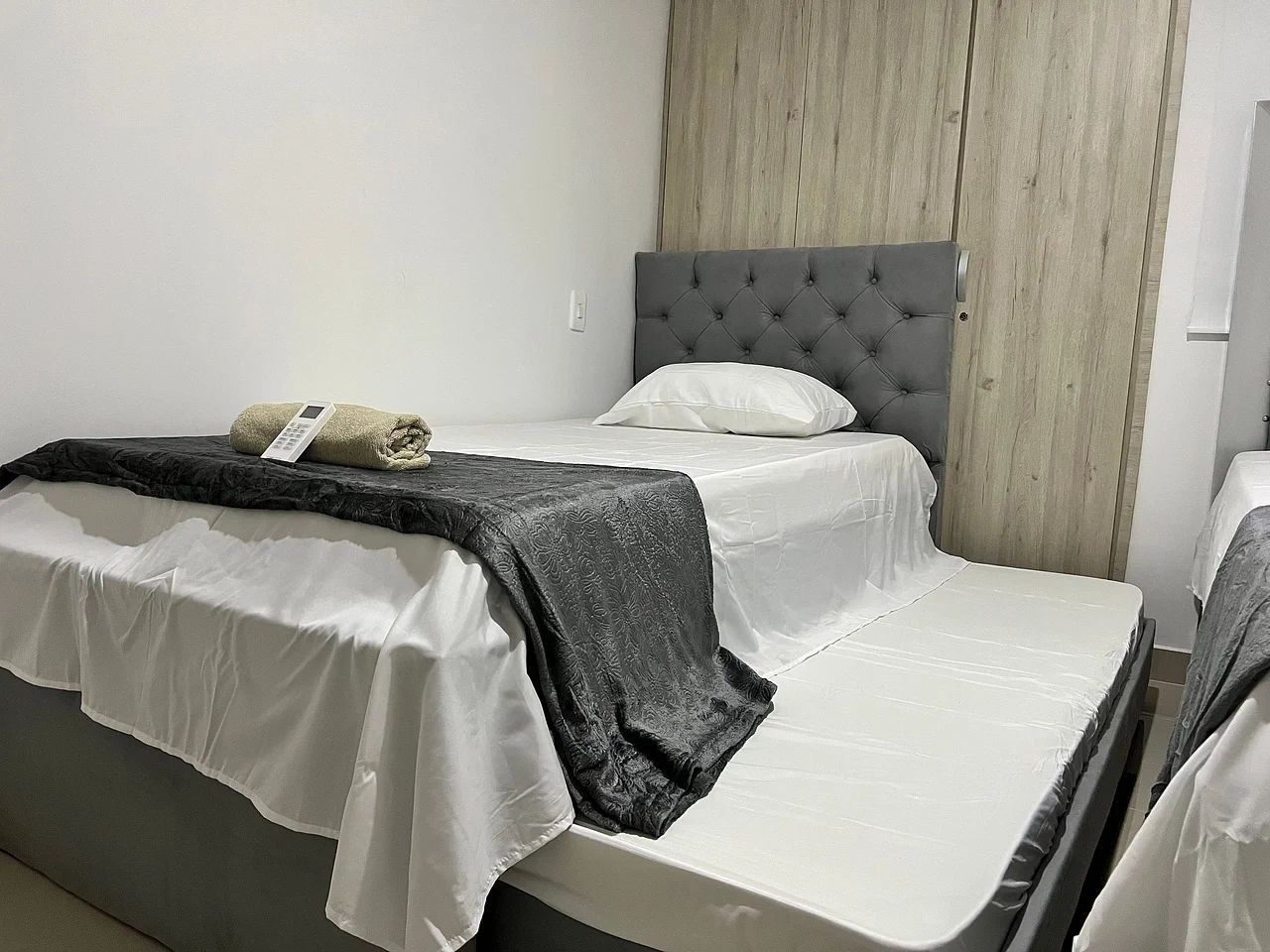 Una cama individual con cabecera gris, colchón blanco y manta gris.