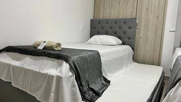 Una cama individual con cabecera gris, colchón blanco y manta gris.
