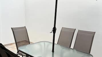 Una mesa con cubierta de vidrio, cuatro sillas y un gran paraguas marrón.