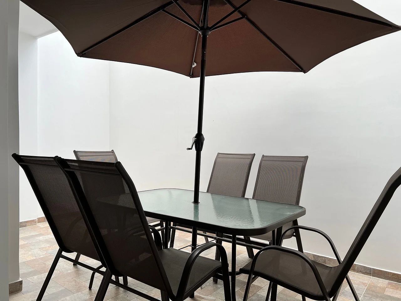 A dining table with four chairs, a large umbrella, and a metal pole.
