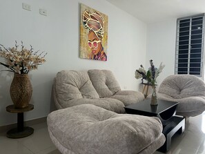 A modern living room with a sofa, armchairs, a coffee table, and a painting on the wall.
