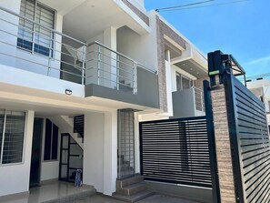 Una casa moderna de dos pisos amb un balcó, una entrada tancada amb reixa i una escala que condueix al pis superior.