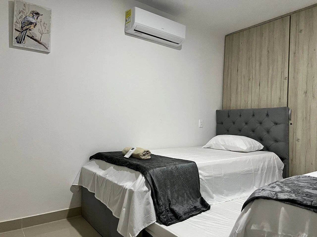 Een slaapkamer met een bed, een nachtkastje, een wandairconditioner en een houten kledingkast.
