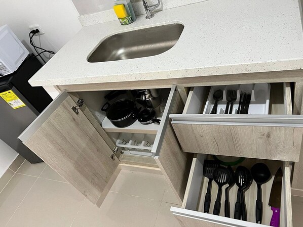 A kitchen with a sink, wooden cabinets, and a drawer with kitchen utensils.