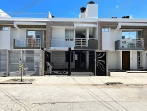 Un immeuble résidentiel moderne à deux étages, doté d’une entrée sécurisée, d’un petit jardin et offrant une vue sur un ciel dégagé.