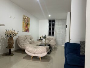 Un saló amb un sofà, una taula de centre i una butaca blava. Hi ha un quadre a la paret i una finestra amb reixatge metàl·lic.