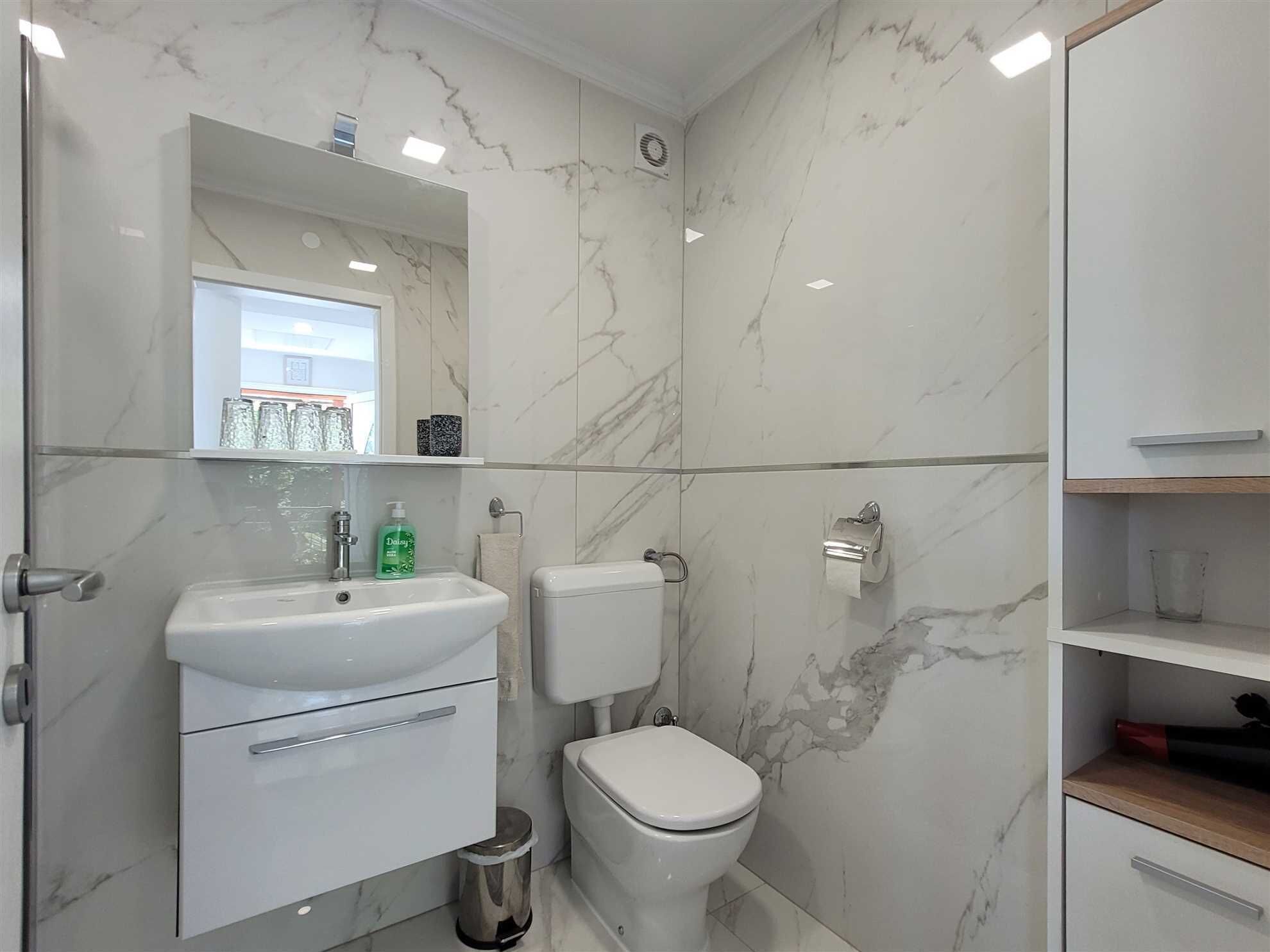 A modern bathroom with a white sink, toilet, and marble walls.