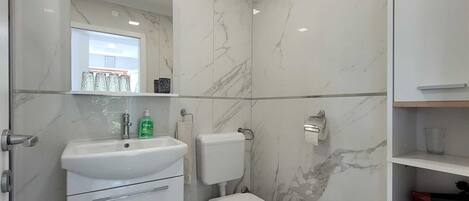 A modern bathroom with a white sink, toilet, and marble walls.
