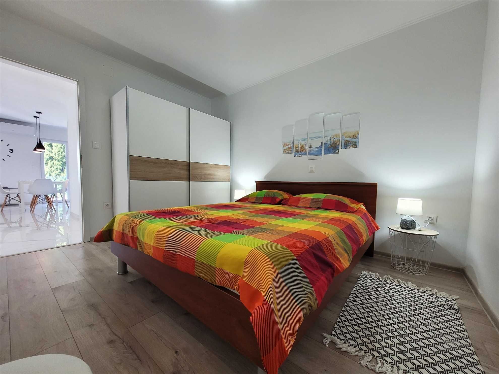 A modern bedroom with a large bed, a bedside table with a lamp, and a view of a balcony.