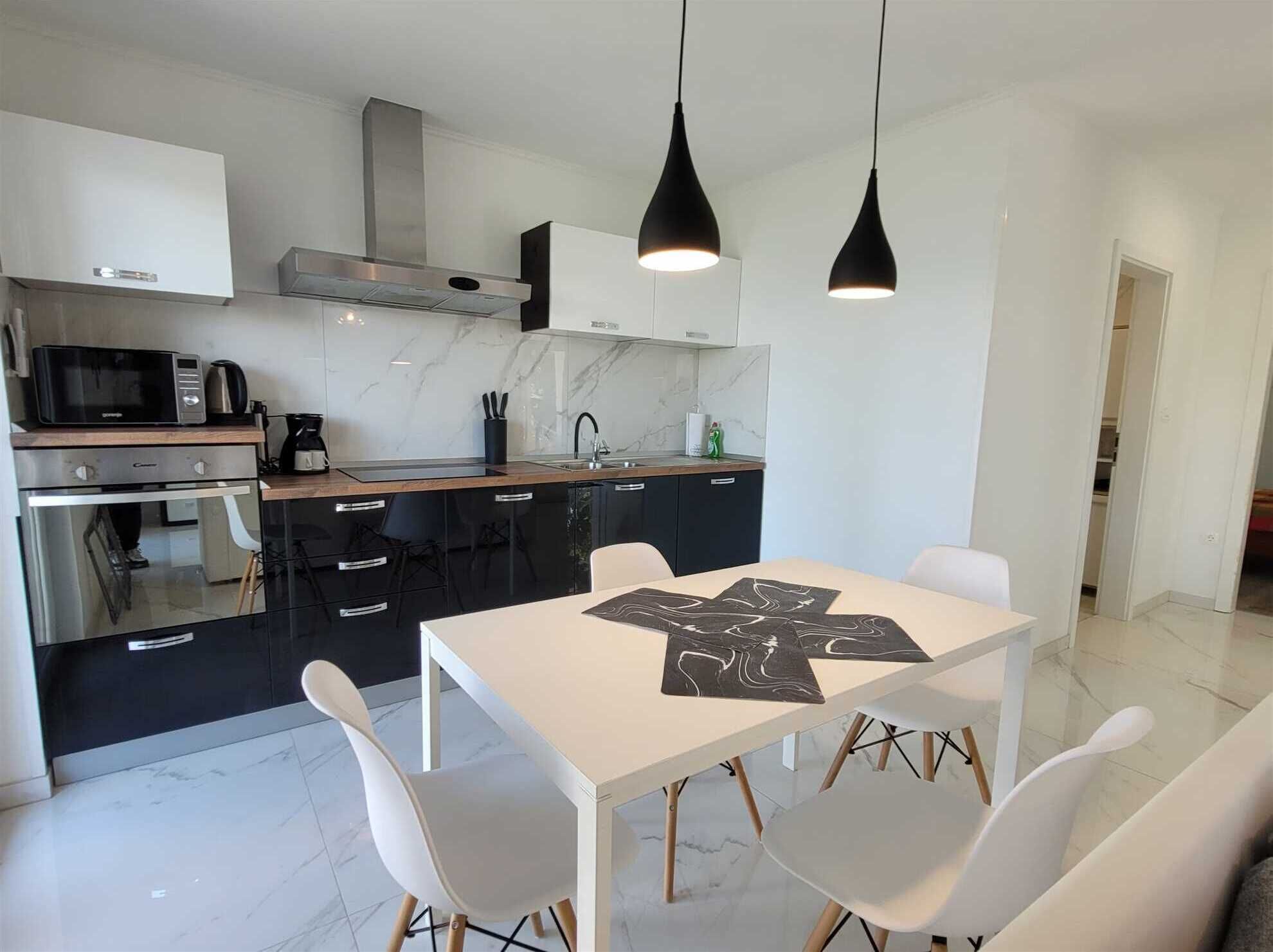 A modern kitchen with a dining area, featuring a white table, black cabinets, and pendant lighting.